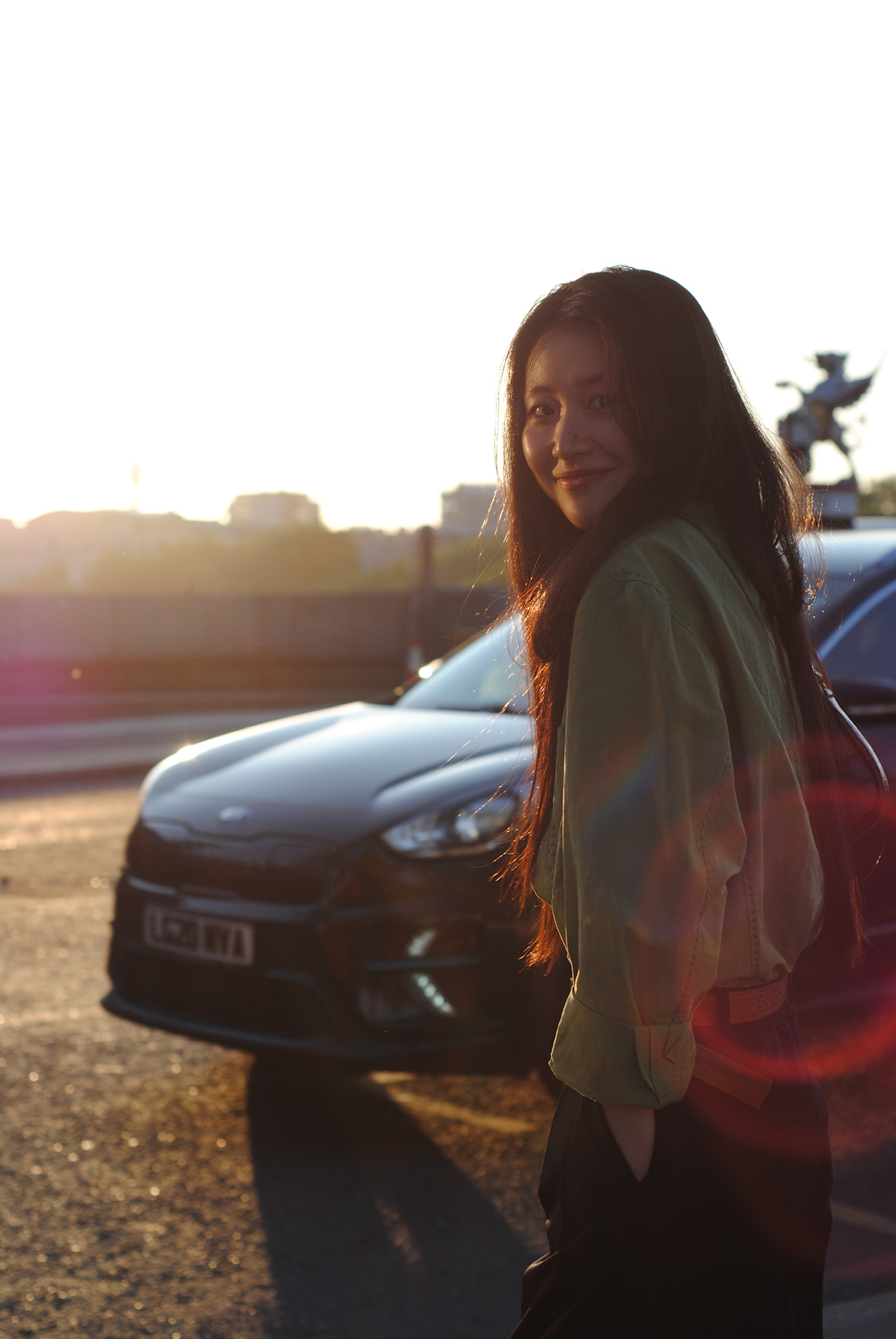 Young woman beside car at sunset with lens flares